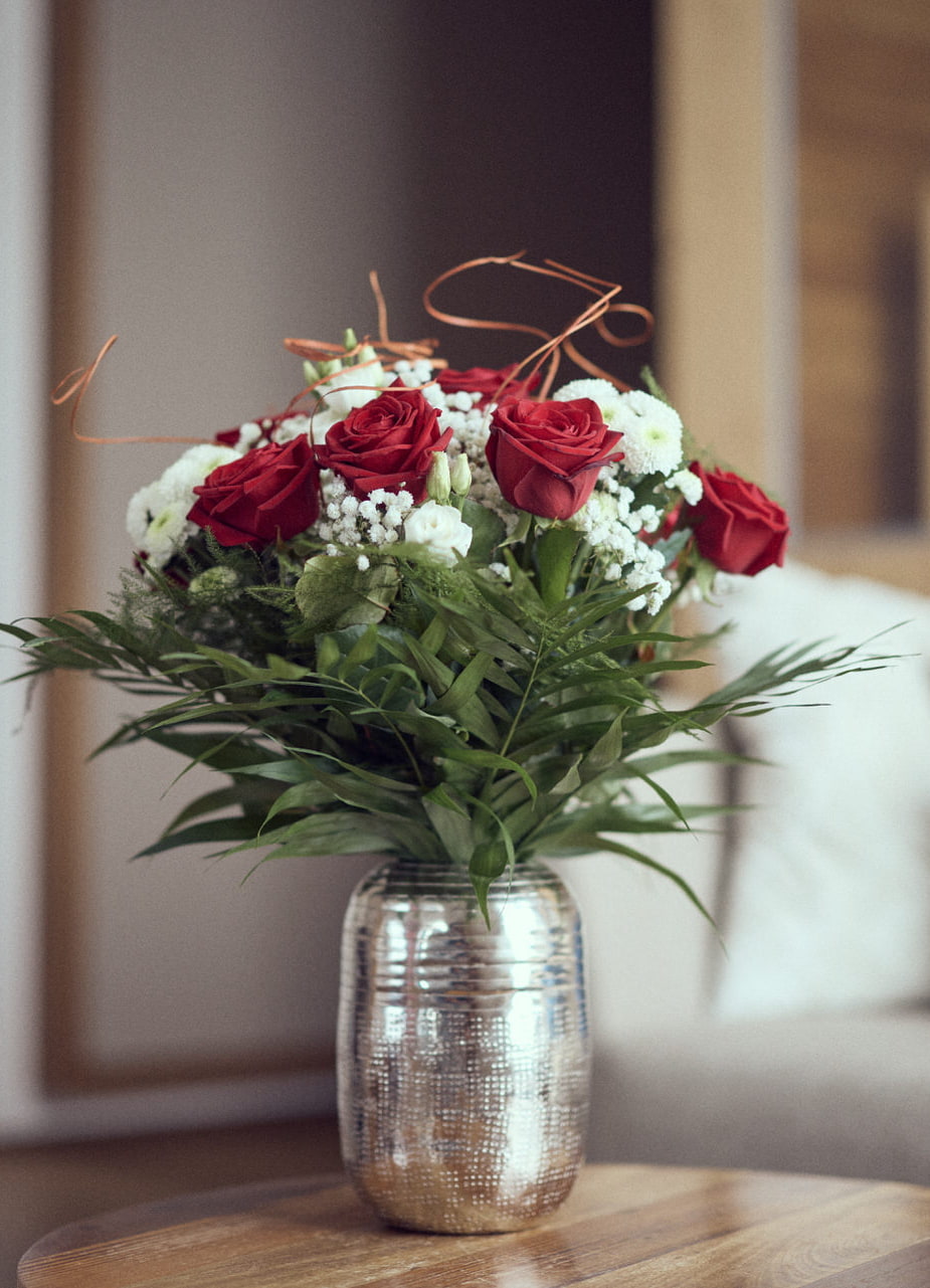 Eine Vase mit langstieligen, roten Rosen auf einem Beistelltisch in einer Suite des Hotel Guglwald.