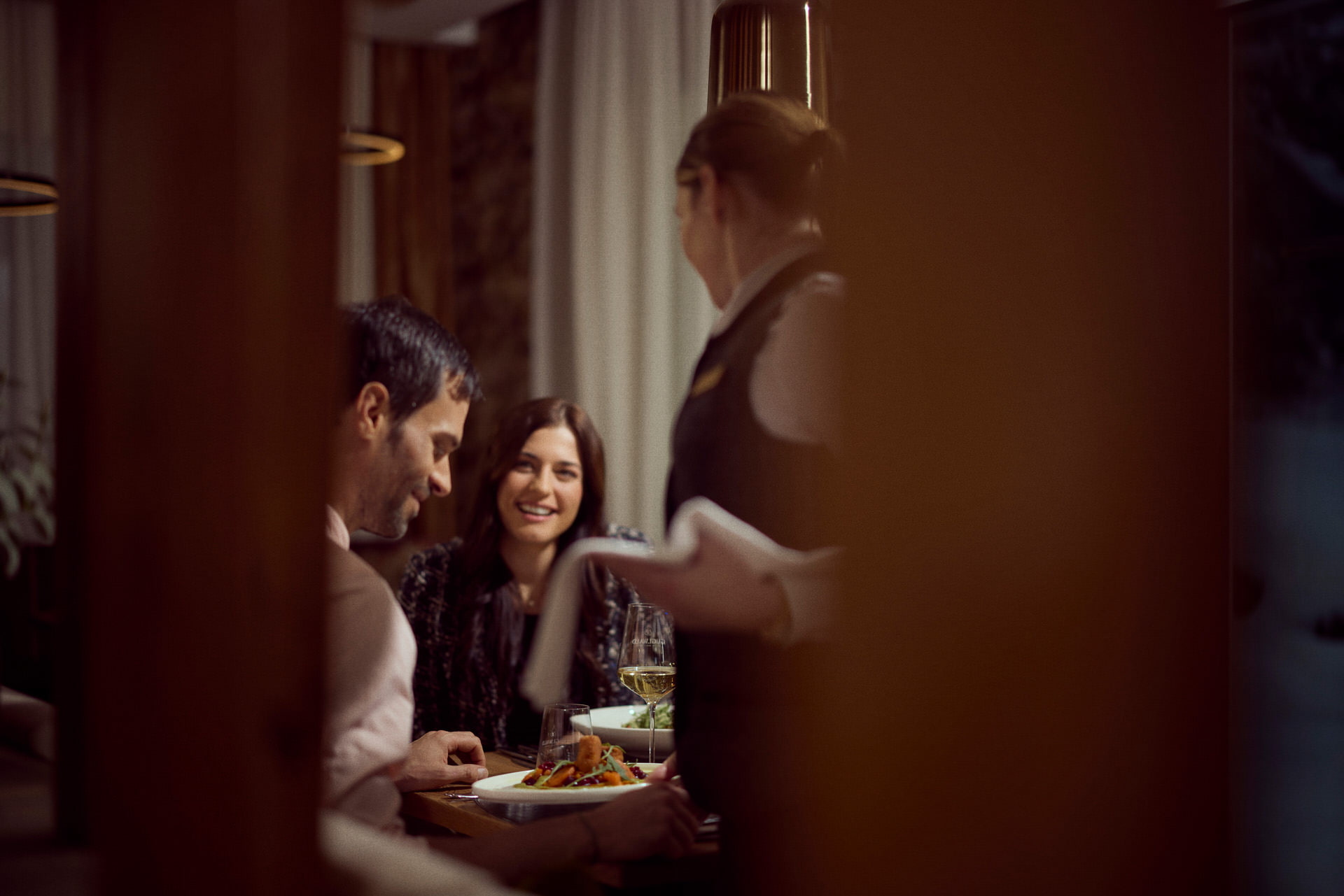 Guglwald Gourmetdinner Zwei Personen bekommen von einer Guglwald-Servicemitarbeiterin ihr Abendessen serviert.